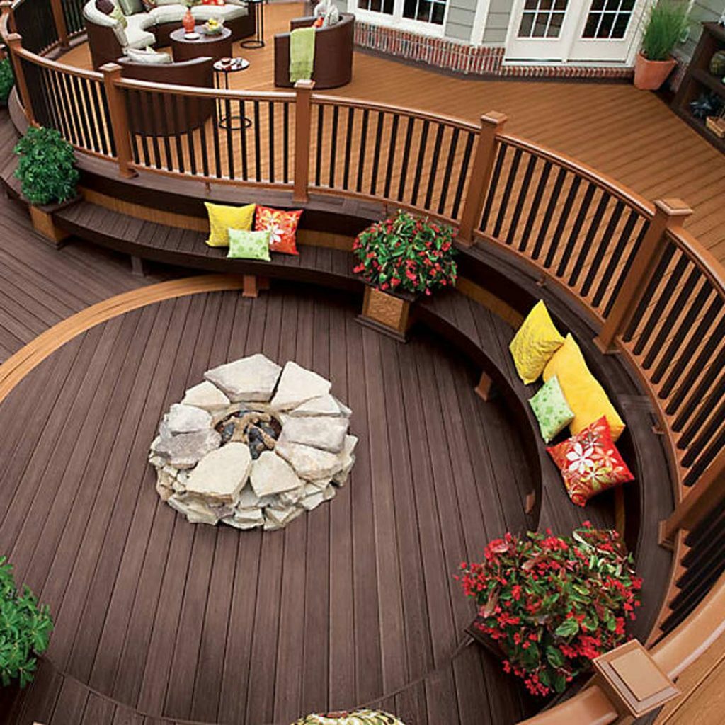 Beautiful curved deck with a fireplace, pillows and flowers. A great example of your decking brands.