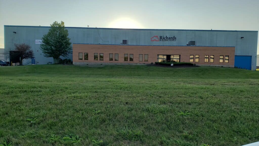 Location photo of our Carol Stream, IL building. This is a wide gray warehouse type building with a brown office entry way with green grass in front.