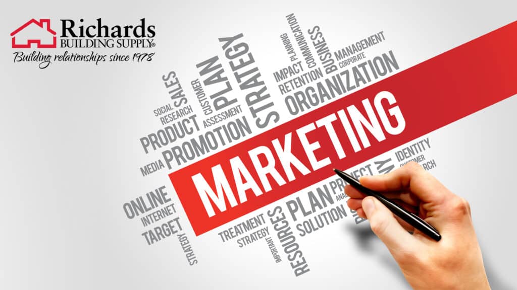 Hand holding a pen that is pointing the word marketing on a graphic with a variety of other words including, business, intentions, communication, strategy, etc...