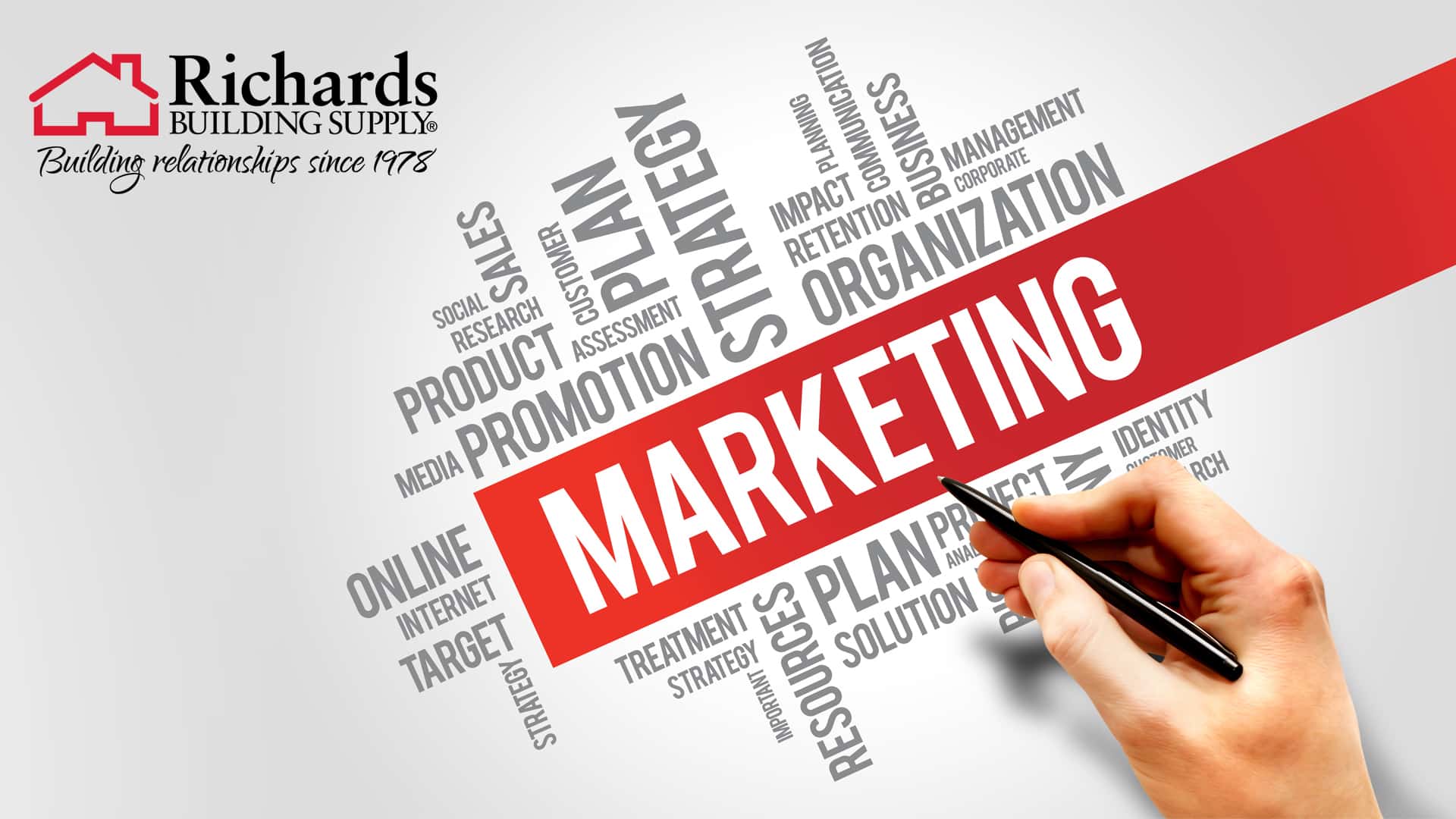Hand holding a pen that is pointing the word marketing on a graphic with a variety of other words including, business, intentions, communication, strategy, etc...