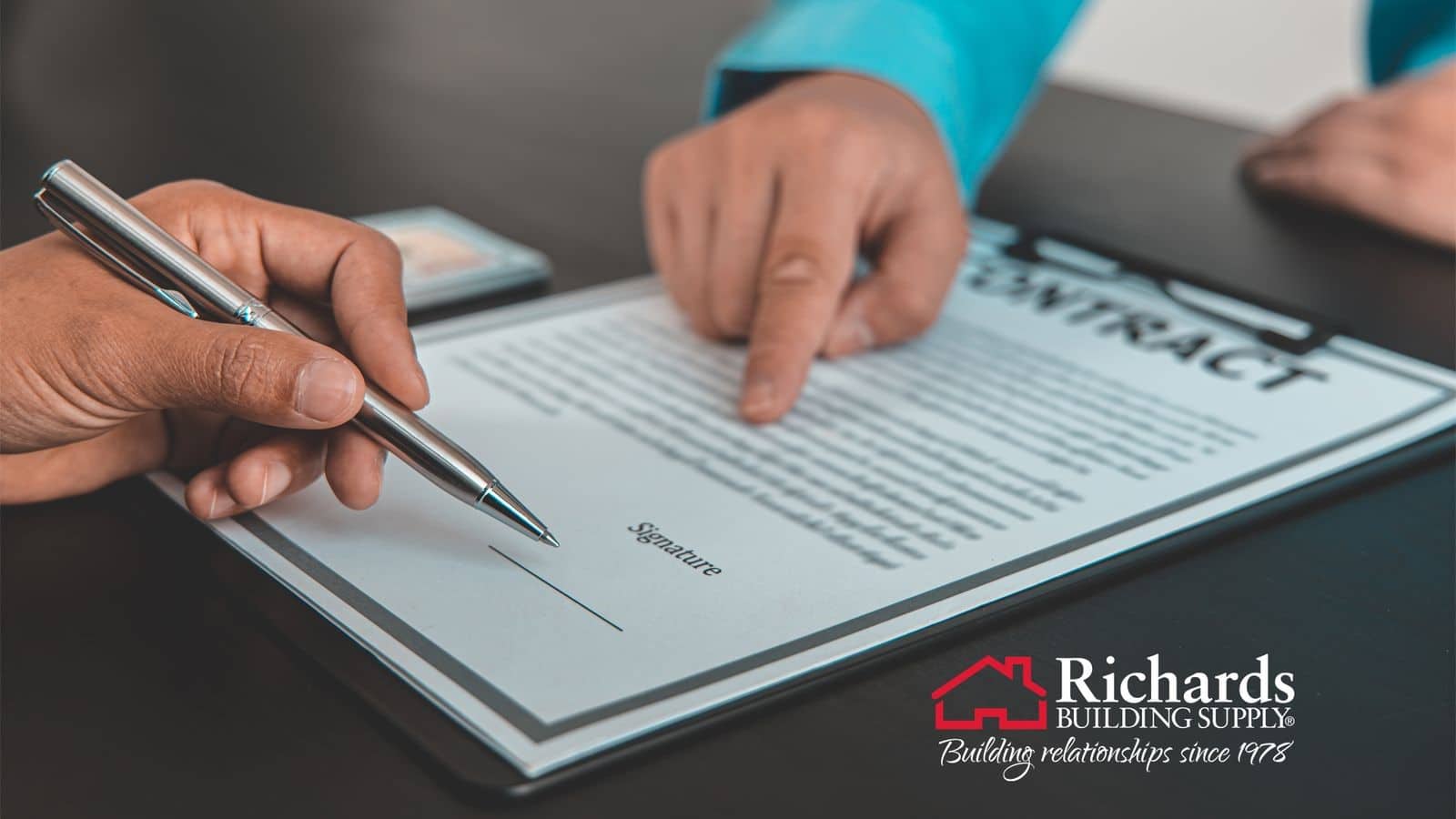 Close up of 2 hands on top of a contract, one holding a pen, the other pointing to where to sign