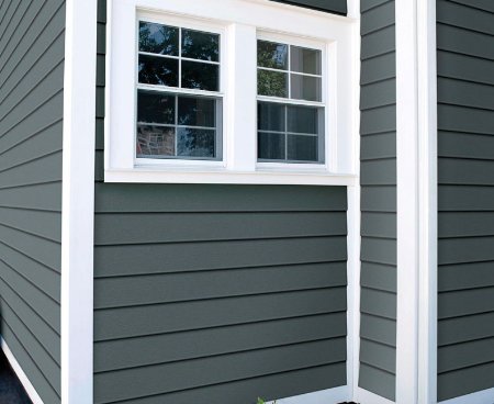 Close up of a house gray siding and white trim around the windows and corners.