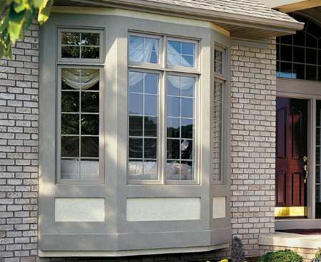An exterior shot of bay type windows installed against on brick wall.