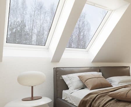 Top floor bedroom with skylight windows next to a bed and lamp.