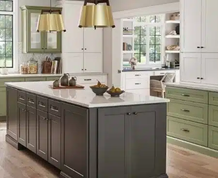 Light green kitchen cabinets, dark gray island with white marble top. gold hanging lamp