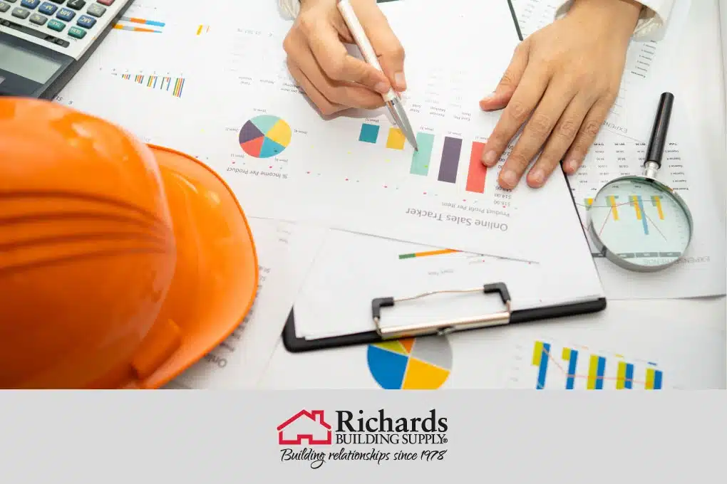 Hands with a pen, on a desk, next to an orange hard hat estimating a project.