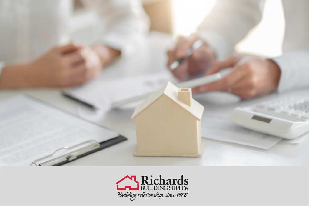2 pairs of hands sitting at a desk, paperwork and a small model home in the foreground.